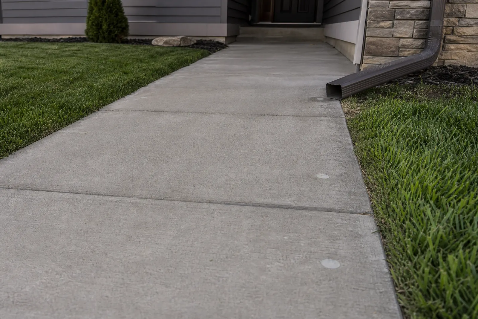 Level concrete walkway beside a lawn and downspout