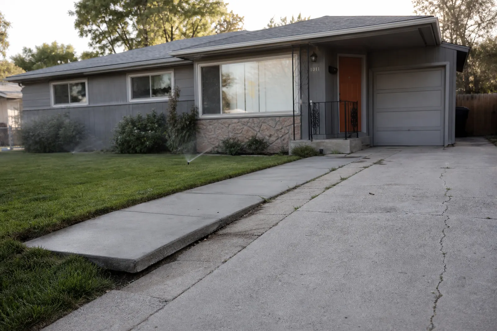 Older single-story home with a settled driveway strip and cracked slab