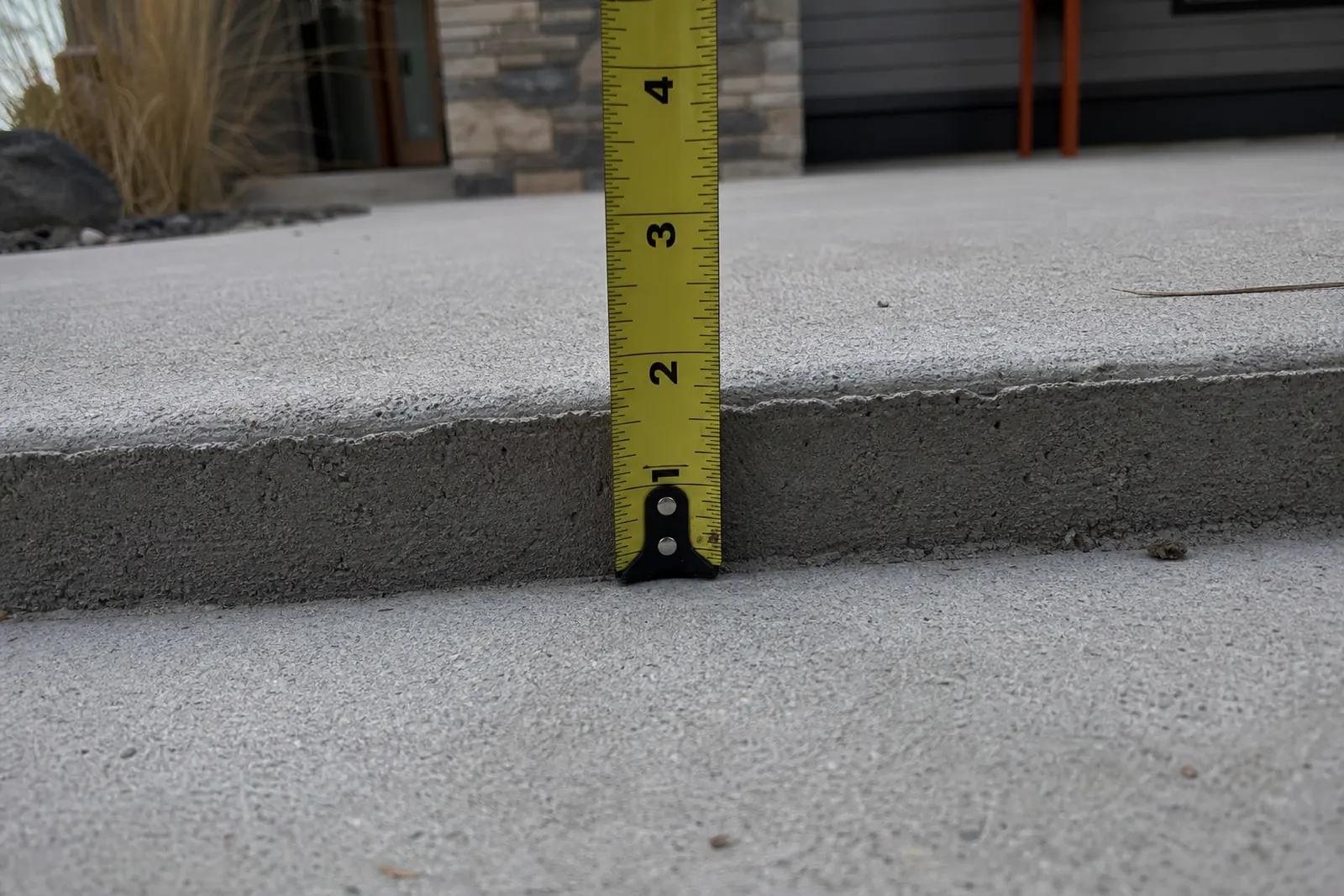 Tape measure showing the height of a lip between two sidewalk slabs